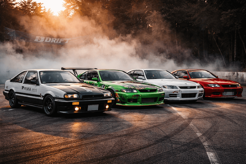 รถ drift ญี่ปุ่น ระดับตำนานหลายคัน เช่น Nissan Skyline และ Toyota AE86 จอดเรียงในสนามดริฟต์ ท่ามกลางควันยางและบรรยากาศการแข่งขันสไตล์ JDM 🚗💨🇯🇵