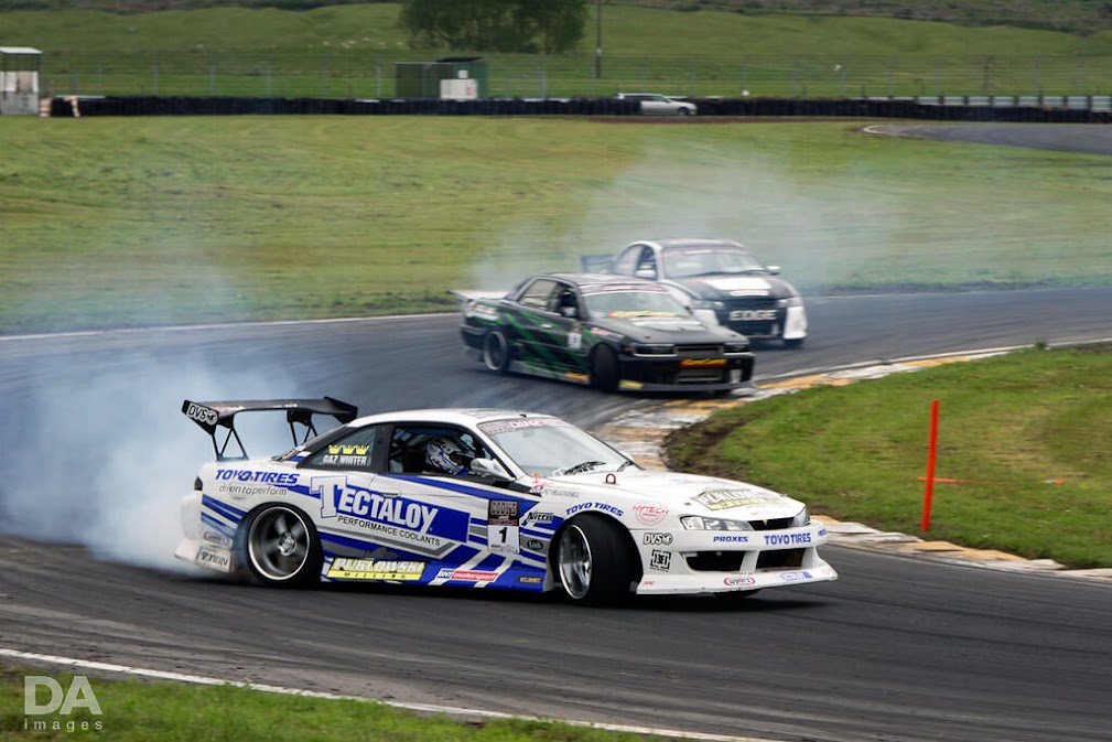 รถ drift ญี่ปุ่น Nissan Silvia S15 กำลังดริฟต์เข้าโค้งในสนามแข่ง มีควันยางด้านหลัง พร้อมรถดริฟต์คันอื่นตามมา แสดงถึงการแข่งขันดริฟต์สไตล์ญี่ปุ่น 🚗💨🇯🇵