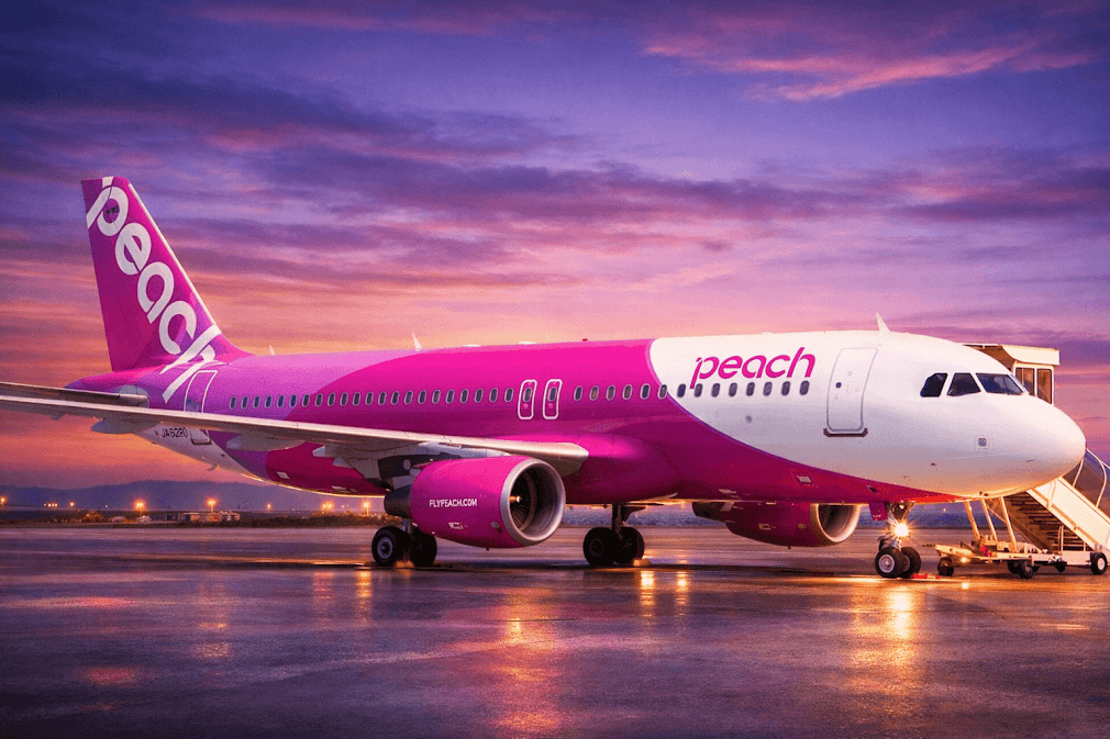 สายการบินของญี่ปุ่น Peach Aviation เครื่องบินสีชมพูจอดอยู่บนรันเวย์ในช่วงพระอาทิตย์ตก พร้อมแสงสะท้อนบนพื้นและบันไดขึ้นเครื่องที่สนามบิน ✈️🇯🇵