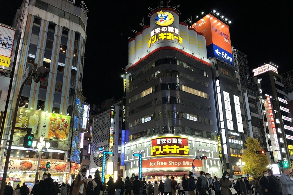 ที่เที่ยว Shinjuku โตเกียว บรรยากาศยามค่ำคืนในย่านชินจูกุ พร้อมแสงไฟนีออนและอาคารเมืองใหญ่ สะท้อนความคึกคักของแหล่งท่องเที่ยวยอดนิยมในโตเกียว