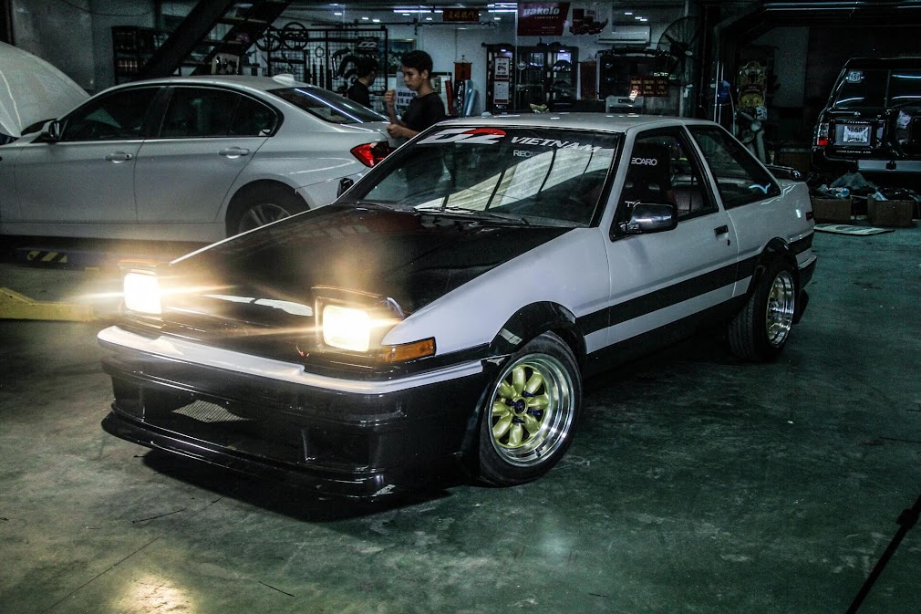 Toyota AE86 รถดริฟต์ในตำนานสไตล์ JDM สีขาวดำ ไฟป๊อปอัพเปิดอยู่ จอดในอู่รถพร้อมชุดแต่งสายซิ่ง