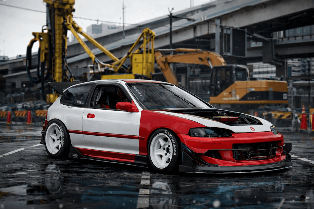 kanjozoku คืออะไร มีที่มาอย่างไร — ภาพรถแต่งสไตล์ Honda Civic สีแดงขาว โหลดเตี้ย ใส่ล้อขาวและชุดแอโร่พาร์ท จอดในเขตก่อสร้างเมืองญี่ปุ่น สะท้อนวัฒนธรรมแก๊งรถซิ่งคันโจโซกุที่มีต้นกำเนิดจากการแข่งบนทางด่วนวงแหวนโอซาก้า (Kanjo Loop)