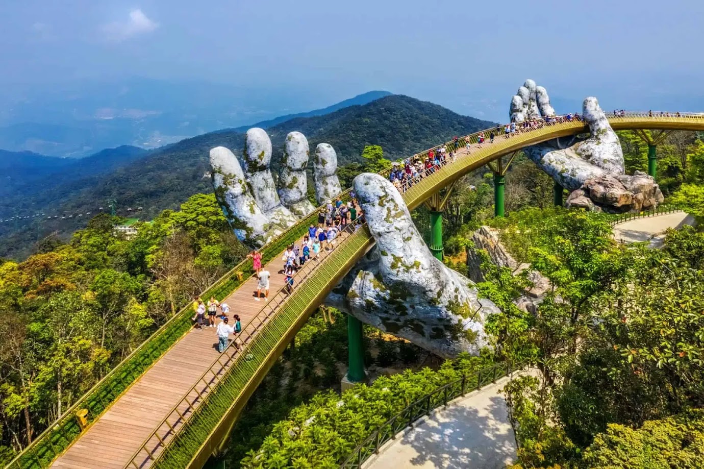 ที่เที่ยวเวียดนาม: สะพานมือยักษ์ (Golden Bridge) กลางภูเขาบานาฮิลส์ มีโครงสร้างสีทองถูกพยุงด้วยรูปปั้นมือหินขนาดใหญ่ รายล้อมด้วยป่าเขียวขจีและวิวภูเขา พร้อมนักท่องเที่ยวเดินชมวิวบนสะพาน