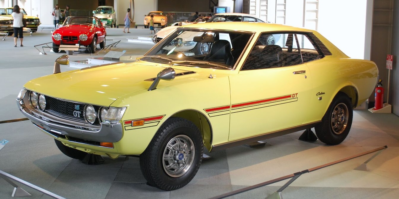 Toyota Celica รุ่นคลาสสิกสีเหลืองสไตล์วินเทจ จัดแสดงในพิพิธภัณฑ์รถยนต์ ดีไซน์ทรงเหลี่ยมยุค 70 พร้อมไฟหน้ากลมและสติกเกอร์ GT ด้านข้าง สะท้อนเอกลักษณ์ความสปอร์ตของ toyota celica ในตำนาน