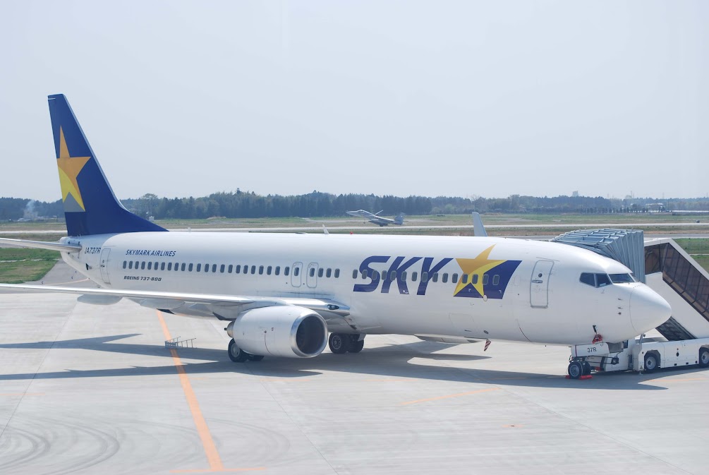 สายการบินของญี่ปุ่น Skymark Airlines เครื่องบิน Boeing 737 จอดอยู่ที่ลานจอดเครื่องบินในสนามบินญี่ปุ่น พร้อมอุปกรณ์ภาคพื้นและบันไดขึ้นเครื่อง ✈️🇯🇵