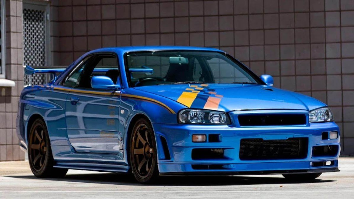 Toyota Supra vs Nissan Skyline comparison concept featuring a blue Nissan Skyline R34 with racing stripes, parked in an urban setting, highlighting iconic Japanese sports car design and performance rivalry