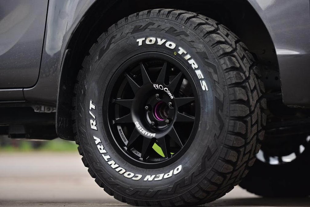 ภาพยางรถยนต์ Toyo Tires รุ่น Open Country R/T ติดตั้งบนรถออฟโรด โชว์ดอกยางลุยและล้อแม็กสีดำ สื่อถึง ยี่ห้อยางญี่ปุ่นยอดนิยม ที่เหมาะกับการใช้งานสมบุกสมบันและทางวิบาก