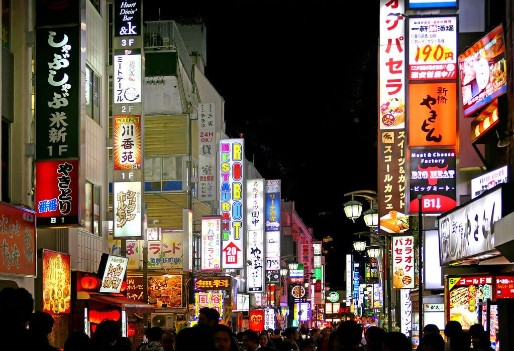 ภาพบรรยากาศยามค่ำคืนใน ย่าน kabukicho เขตชินจูกุ โตเกียว ประเทศญี่ปุ่น เต็มไปด้วยป้ายไฟนีออนสีสันสดใส ร้านอาหาร บาร์ และสถานบันเทิง ผู้คนเดินพลุกพล่านบนถนนสายดัง สะท้อนเสน่ห์ไนท์ไลฟ์และความคึกคักของ ย่าน kabukicho ในโตเกียวยามค่ำคืน